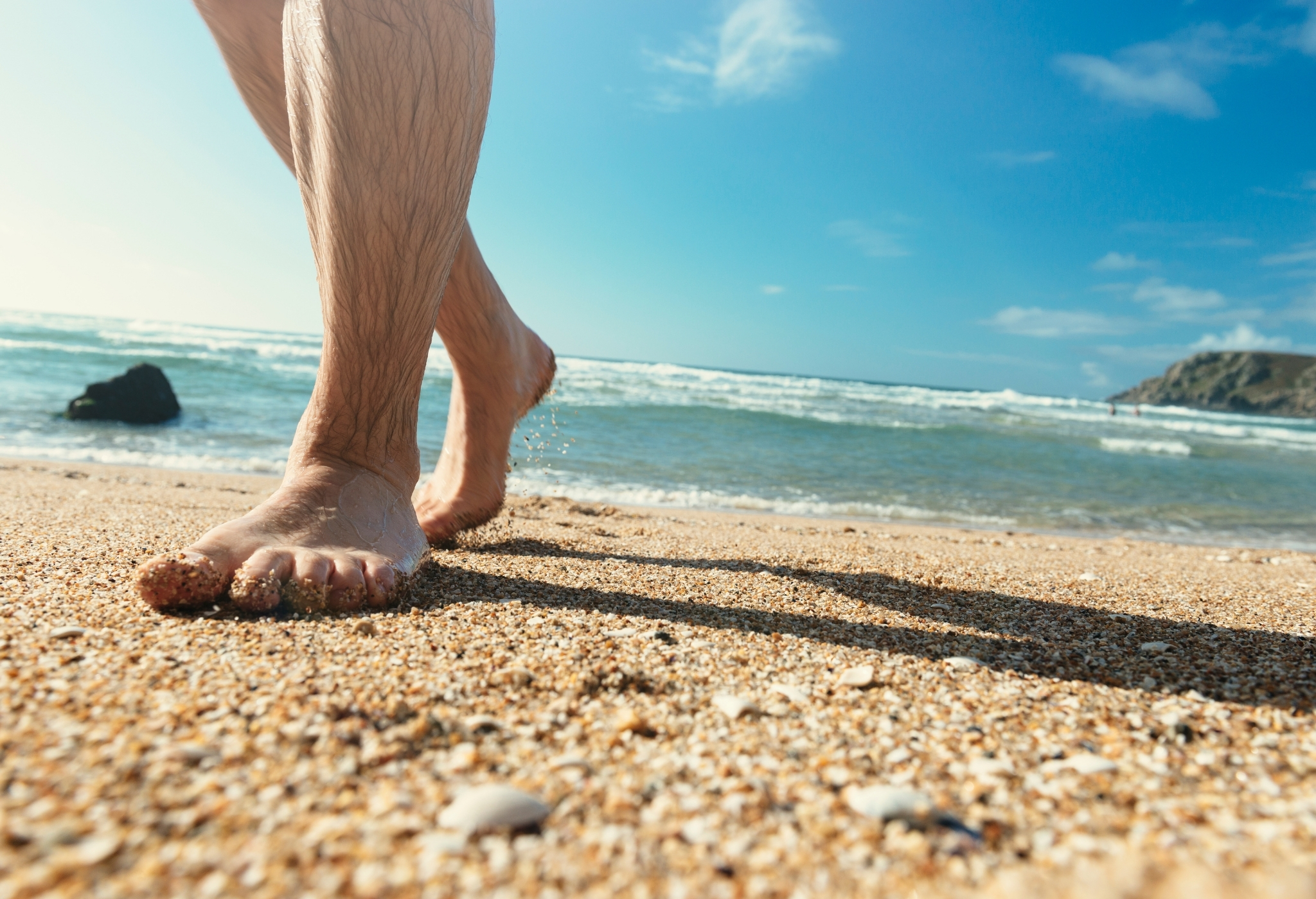 человек идет по пляжу с волосатыми ногами