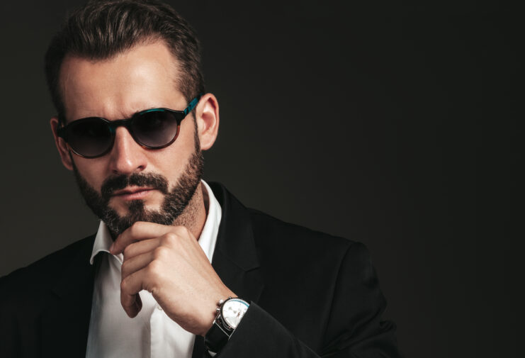 closeup-portrait-handsome-confident-stylish-hipster-lambersexual-model-sexy-modern-man-dressed-elegant-black-suit-fashion-male-posing-studio-dark-background-sunglasses