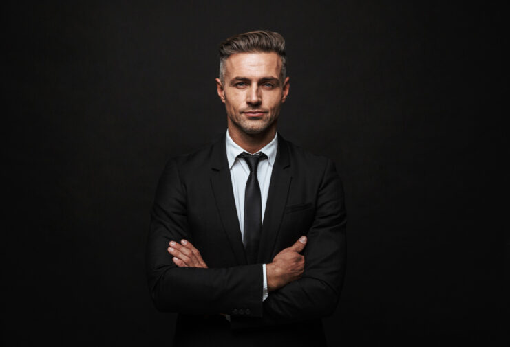 handsome-confident-businessman-wearing-suit-standing-isolated-black-wall-arms-folded