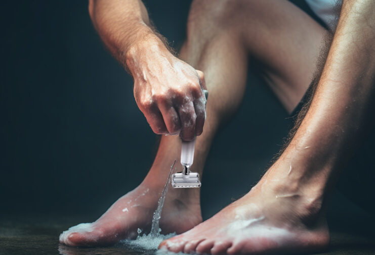 man shaving legs with safety razor